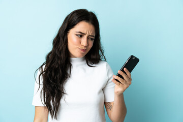 Young woman using mobile phone isolated on blue background with sad expression