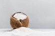 Coco abierto lleno de coco rallado que se derrama sobre una mesa blanca