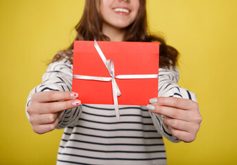 Happy young teenager girl holds red gift certificate on yellow background. People lifestyle holidays concept.