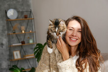 Portrait Of Young Woman In The Living Room At Home With A Cute Siberian Cat. Female Hugging Her Long Hair Kitty. Background, Copy Space, Close Up. Adorable Domestic Pet Concept.