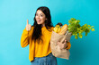 © luismolinero - Young woman holding a grocery shopping bag isolated on blue background giving a thumbs up gesture