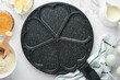 Empty frying pan black, skillet with stone nonstick coating for baking pancakes in shape of breakfast hearts and ingredients on gray concrete table background. Breakfast for Valentines Day. Top view.