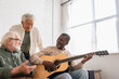 © LIGHTFIELD STUDIOS - Smiling african american man playing acoustic guitar near interracial friends at home.