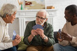 © LIGHTFIELD STUDIOS - Elderly man holding playing cards near multicultural friends at home.