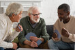Positive interracial pensioners playing cards at home.