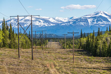 Electricity, Power Lines Seen In Rural Canada During Summertime With Blue Sky, Clouds And Mountains, Boreal Forest Landscape. 