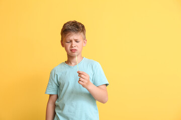 Poster - Displeased little boy in blue t-shirt chewing gum on yellow background