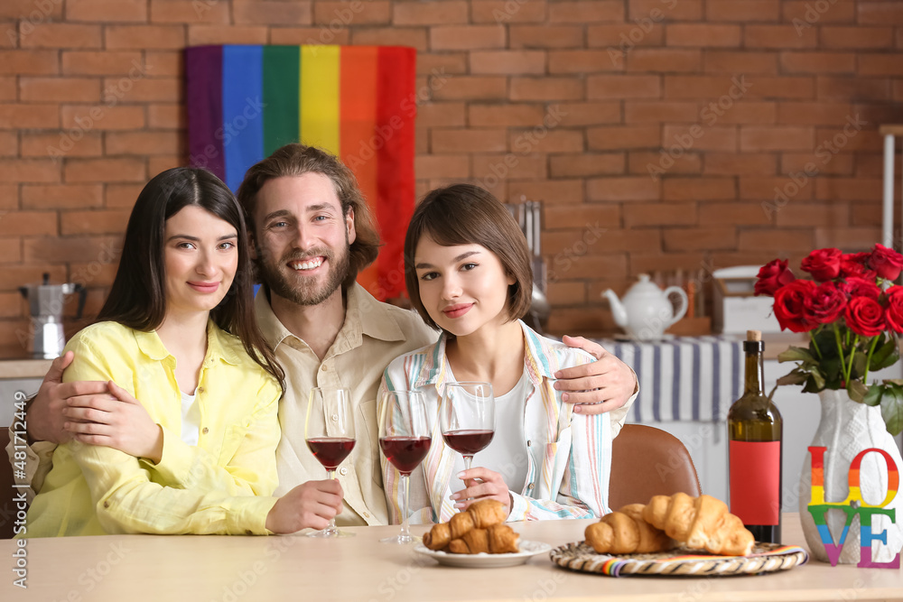 Man and two beautiful women drinking wine at home. Concept of polyamory