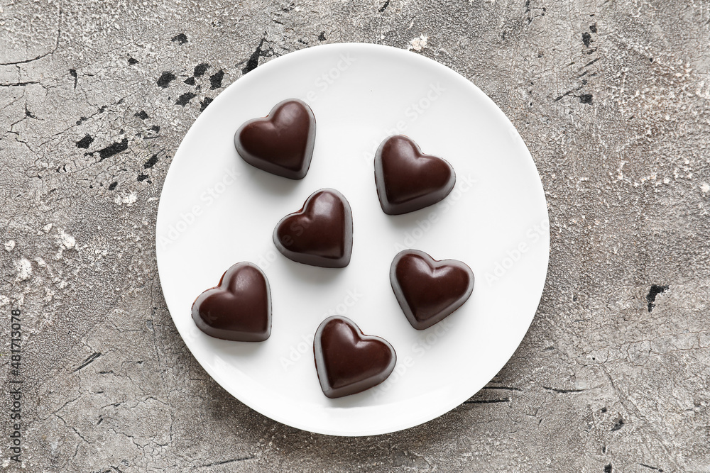 Plate with tasty heart-shaped candies on grey background
