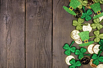 Wall Mural - St Patricks Day side border against a dark wood background. Overhead view with gold coins, shamrocks and leprechaun hats. Copy space.