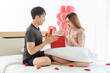 © Montri Thipsorn - Couple Love and Valentine's Day Concept. Young asian man with beautiful giving gift box surprise girlfriend on bed in bedroom with red balloon.