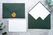 Wedding stationery set. Green envelopes and blank paper card on concrete table with eucalyptus branches.