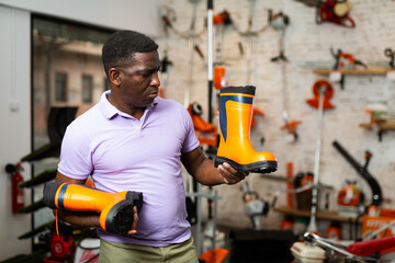 Male shopper chooses rubber boots at a garden tool store