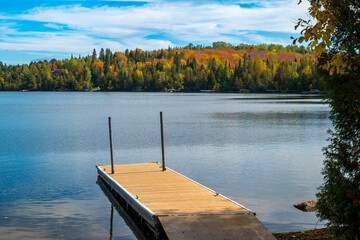  Colorful autumn foliage over Caribou Lake in northern Minnesota, with a boat dock,. beautiful woods and ripples on the blue water on a partly sunny morning.
