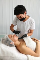 Wall Mural - A beautician gives facial rejuvenation injections to a middle-aged woman.