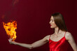 © Roman Kornev - A young woman with long brown hair, in a red dress on a red background with fire