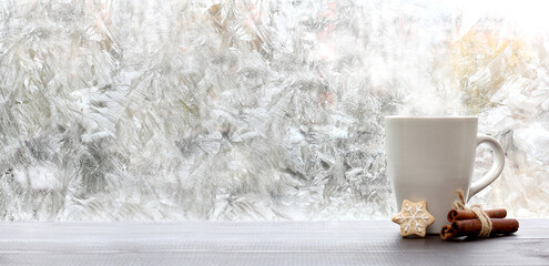 Wall Mural - frosty patterns on the window and a mug of cookies and cinnamon. warming coffee overlooking a winter morning