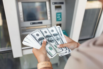 Wall Mural - Young arab woman in hijab withdraws money, counts dollars near atm with blank screen