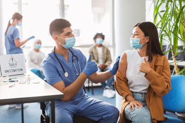 Wall Mural - Vaccinated Asian Lady And Doctor Gesturing Thumbs-Up At Clinic