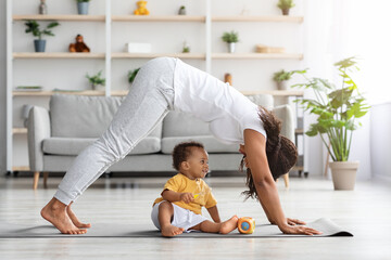 Wall Mural - Young black mother practicing yoga at home with her infant son