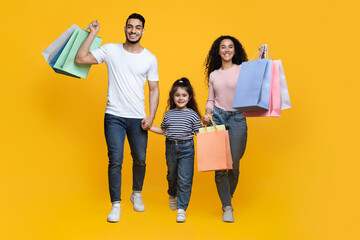 Wall Mural - Happy Cheerful Arab Parents And Their Daughter Walking With Bright Shopping Bags