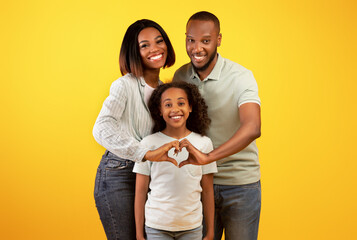 Happy loving family. Black parents holding hands in heart shape sign, posing with liitle daughter over yellow background