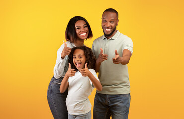 Wall Mural - Hey, you. Excited black parents and their daughter pointing fingers at camera, standing over yellow background