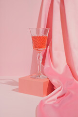 Pastel pink Valentine's Day or birthday composition with wine glass and satin on pastel background. Trendy romantic aesthetic.