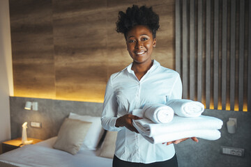 Maid putting stack of fresh white bath towels on the bed sheet. Room service maid cleaning hotel room. Maid making bed in hotel room. Change of towels in the hotel room