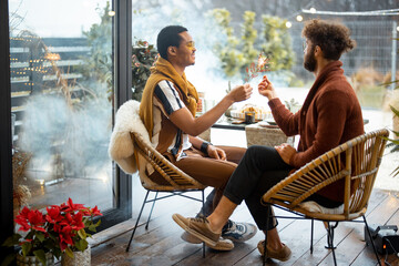 Two male friends having fun burning sparklers, during a festive dinner at backyard. Caucasian and hispanic man celebrating together. Idea of gay couples and holiday mood