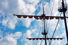 The Masts Of A Sailing Ship Against The Blue Sky And White Clouds