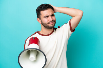 Wall Mural - Young Brazilian man isolated on blue background holding a megaphone and having doubts