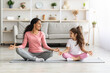 Cheerful mother and daughter meditating together at home