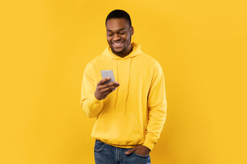 Wall Mural - African American Guy Using Cellphone Texting Standing Over Yellow Background