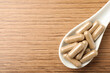 © New Africa - Spoon with dietary supplement capsules on wooden table, top view. Space for text