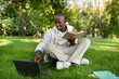 © Prostock-studio - Preparing for exams outdoors. Happy black student guy studying with book and laptop computer, sitting in campus