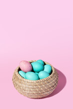 Wicker Basket With Blue Eggs And A Single Pink One On A Pink Background