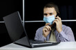 © Oleg - Man in face mask talking on mobile phone sitting at laptop with thoughtful face expression. Discussion of working issues, office call