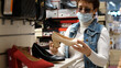 © emaria - Elderly woman in medical mask and eye glasses choosing shoes in a shoe store. Shopping mall, safety during coronavirus pandemic.