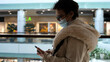 © emaria - Elderly woman in medical mask and eye glasses uses phone while walking in a shopping mall