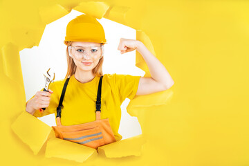 Young blond woman in uniform builder clothes, hardhat is holding metal wrench. Girl worker is looking confident. Repair, building at home, flat concept. Instruments, tools, accessories for renovation.