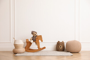 Wall Mural - Rocking horse with bear toy, pouf and wicker baskets near white wall in child room. Interior design