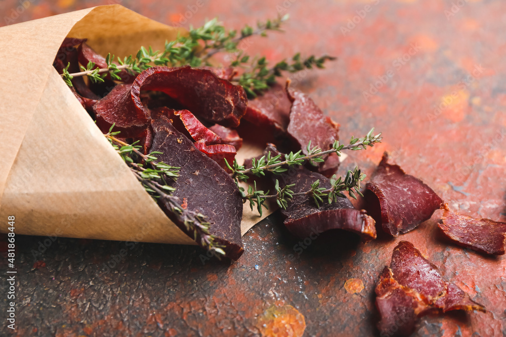Paper bag with spicy beef jerky on color background