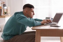 Man With Poor Posture Using Laptop At Table Indoors