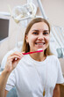 © DSMT - A young woman in a white t-shirt sits in a dental office, smiles and holds a toothbrush in her hands. Girl with braces shows oral care. Dentistry, dental treatment