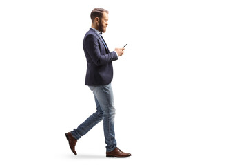 Wall Mural - Full length profile shot of a young man in suit and jeans walking and typing on a mobile phone