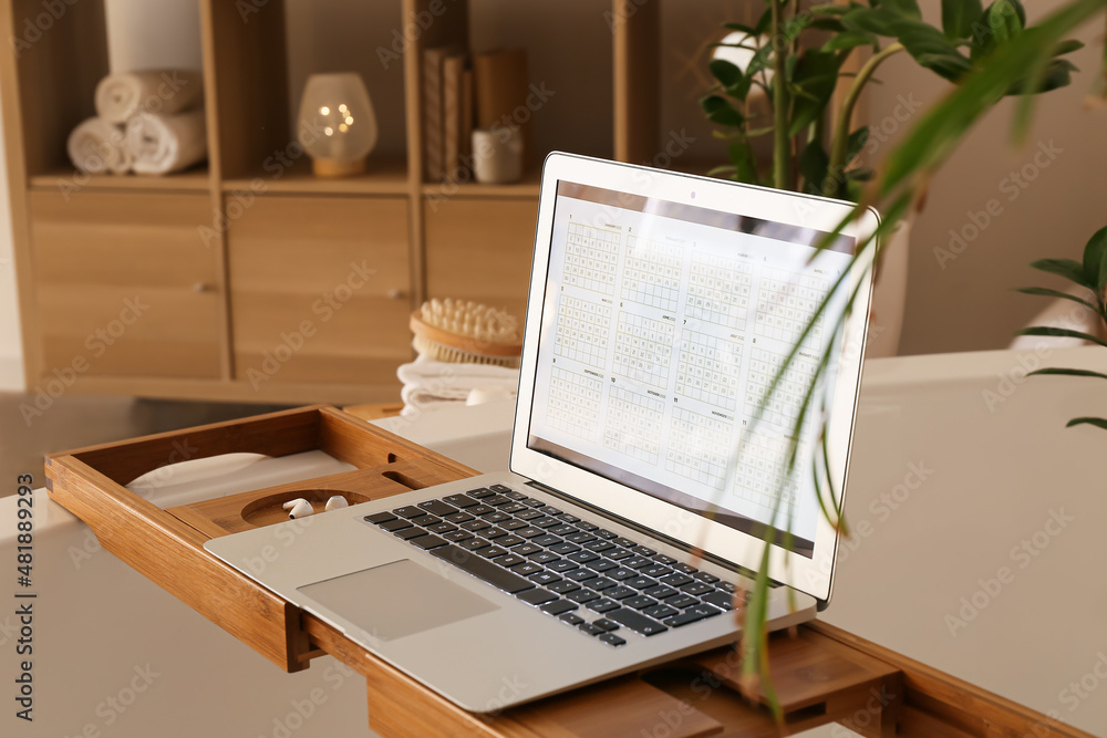 Laptop with digital calendar on tray in bathroom