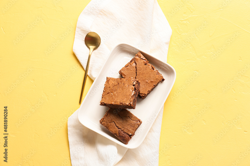 Plate with pieces of tasty chocolate brownie on yellow background