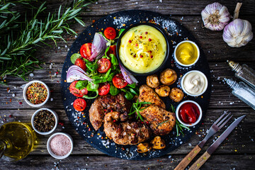 Fried pork steaks with potato puree and vegetable salad served on black stone plate on wooden table
