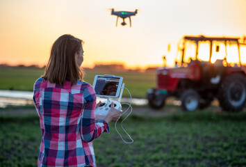 Poster - Agronomist using drone in agriculture standing in field in front of tractor